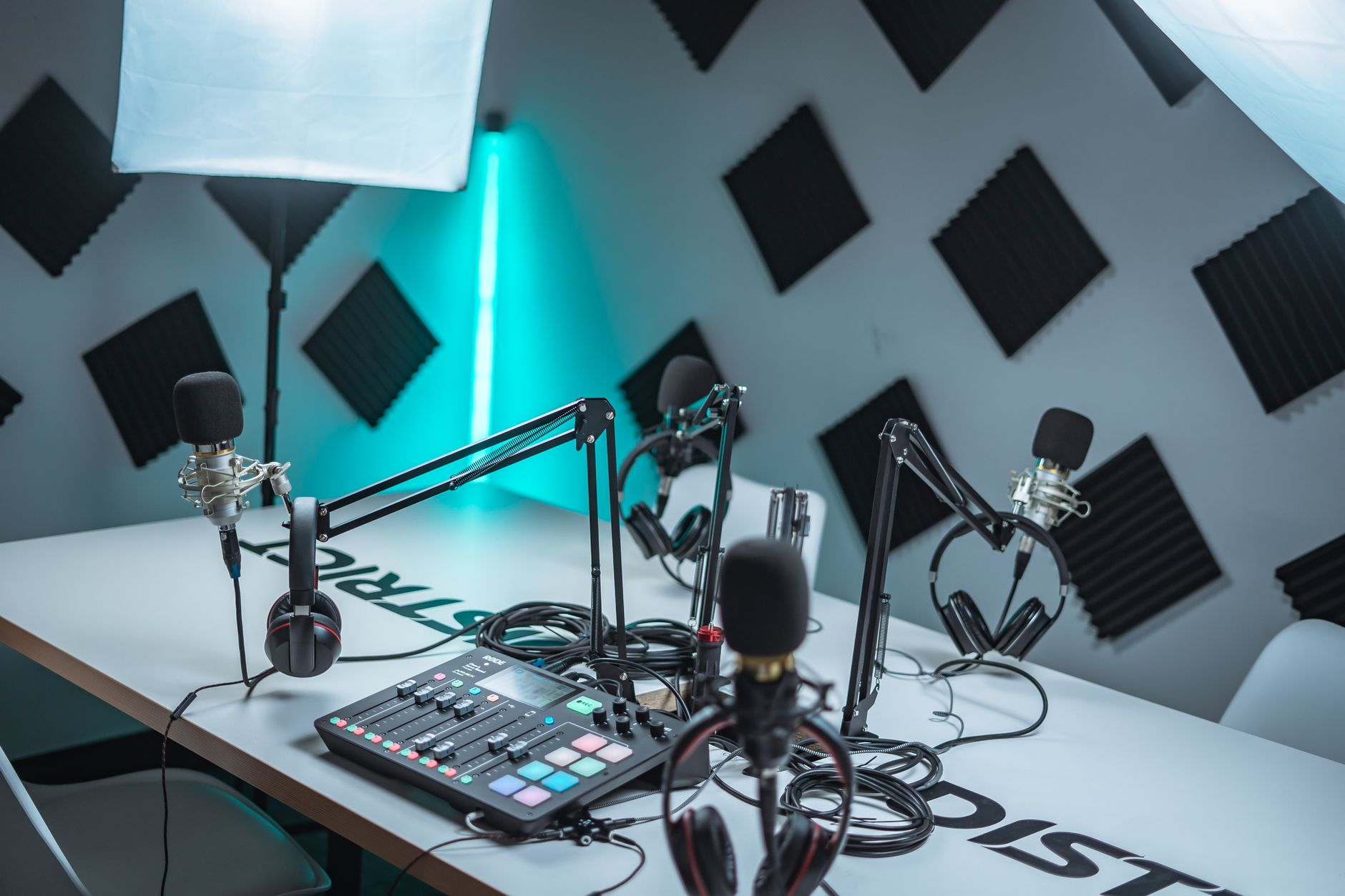 petit studio de radio avec plusieurs micros sur bras articulés, casques et console de mixage posés sur une table blanche