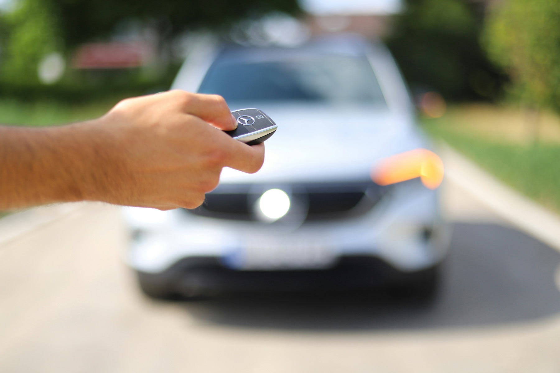 main tenant une clé de voiture avec télécommande, véhicule visible en arrière-plan flou sur une route