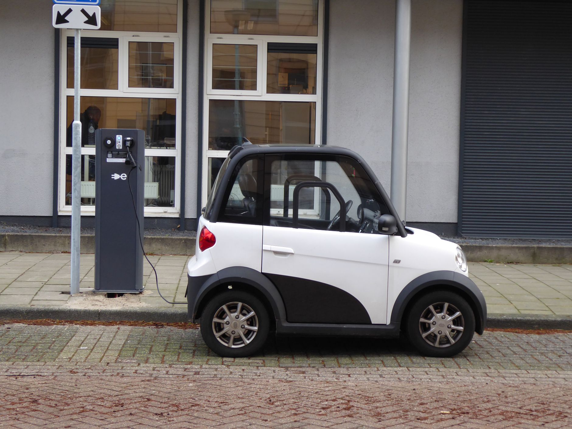 petite voiture électrique blanche et noire branchée à une borne de recharge publique sur un trottoir