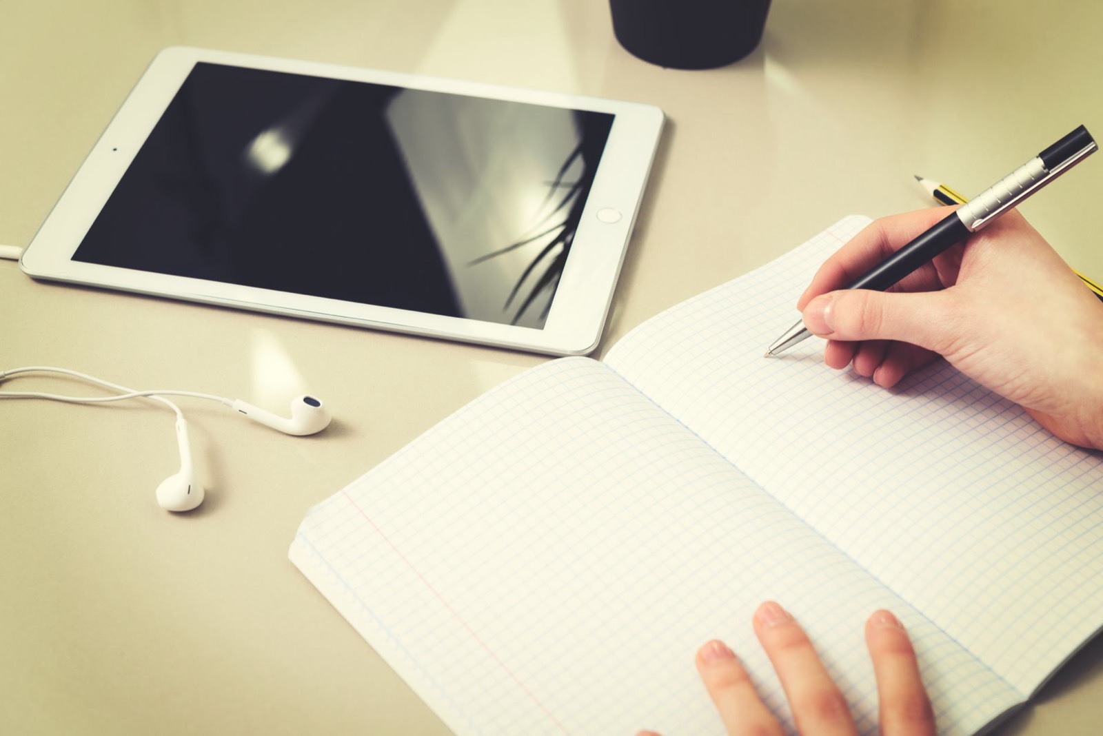 Personne tapant des lettres sur une tablette avec un carnet à côté